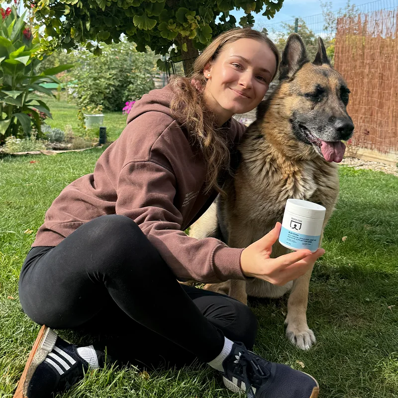Halterin sitzt mit ihrem Deutschen Schäferhund und einer Dose Multi Chew im Garten